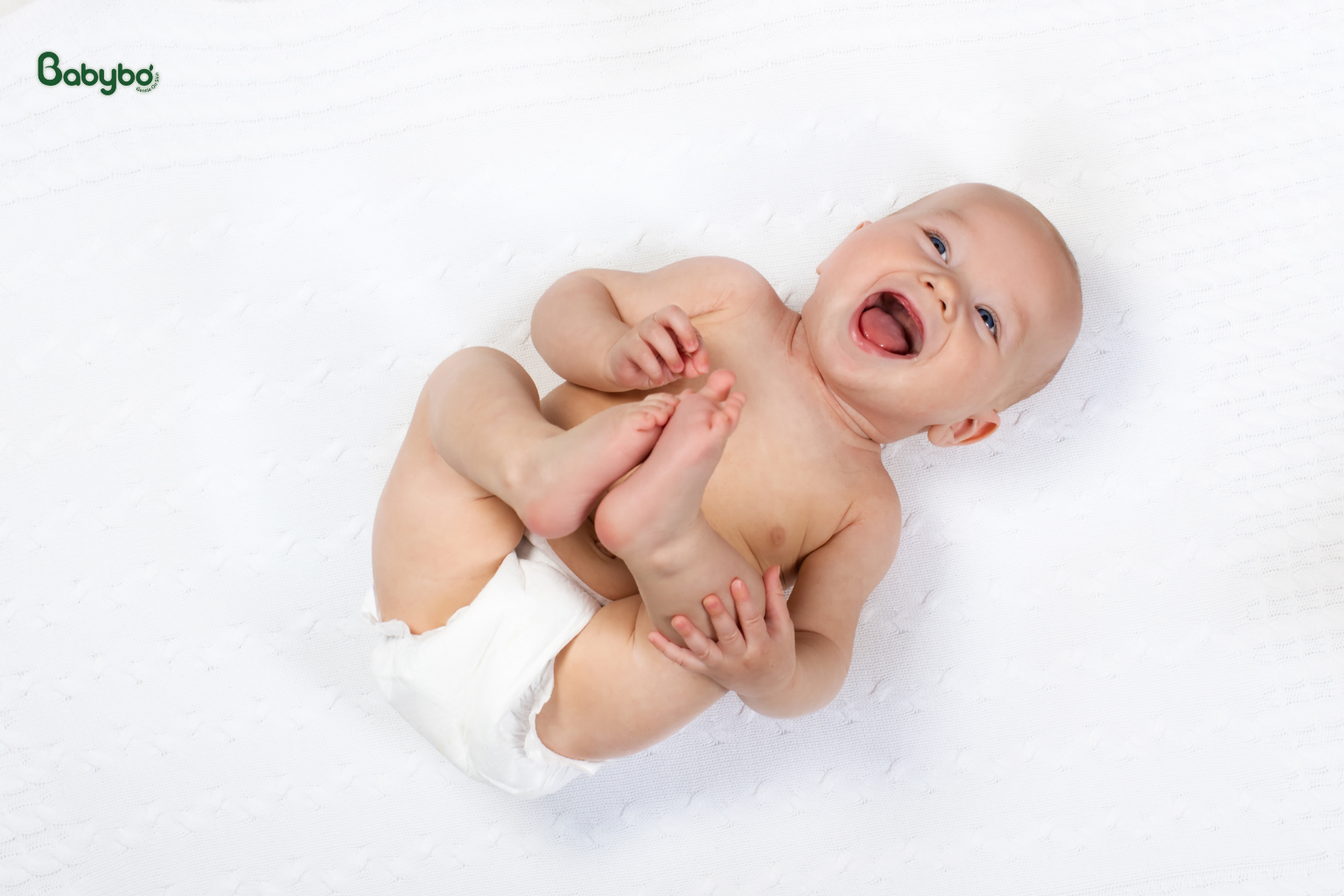 Hình ảnh em bé mặc bỉm nằm vui vẻ trên nền trắng, minh họa làn da bé khỏe mạnh và thoải mái khi được chăm sóc đúng cách.